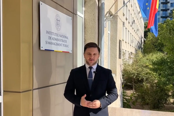 Reprezentant INAMP, surprins în fața sediului Institutului Național de Administrație și Management Public, alături de placa instituției și drapelele Republicii Moldova și Uniunii Europene.